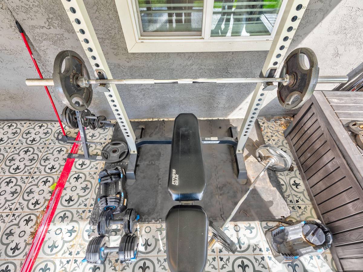 Home gym area with a weight bench, barbell and dumbbells at Pama Lane
