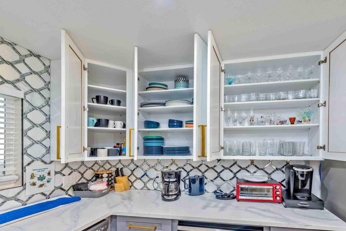 Open kitchen cabinets stocked with dishes and glassware above a coffee station at Pama Lane